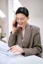 Confident businesswoman wearing glasses, talking on phone while reviewing documents in modern office setting.